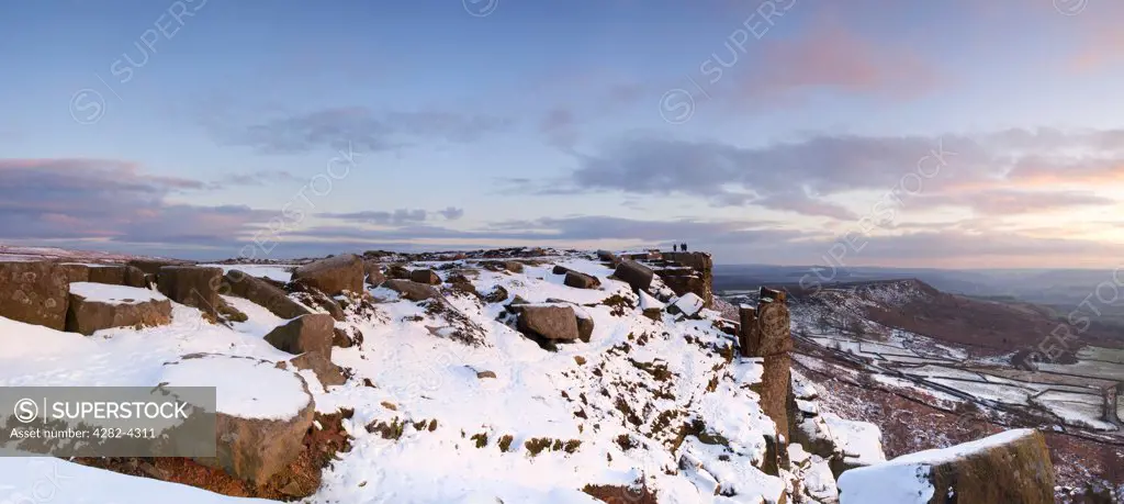 England, Derbyshire, Curbar Edge. Panoramic view of Curbar Edge and the Pinnacle rock illuminated by the last rays of the setting sun in the Peak District National Park following winter snowfall.