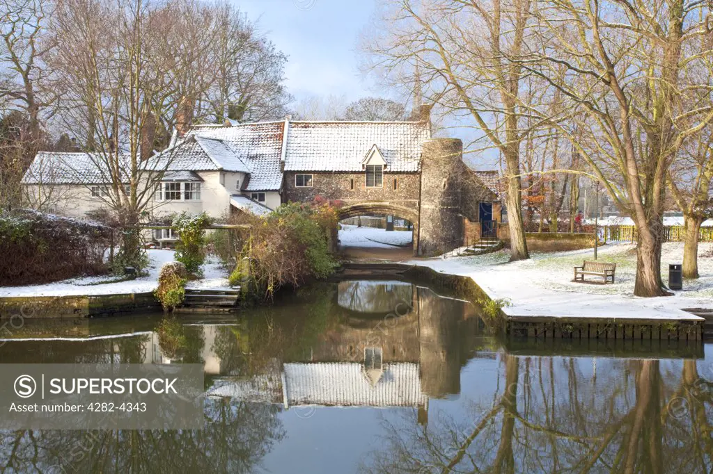 England, Norfolk, Norwich. Pulls Ferry, once a 15th Century watergate, on the River Wensum following winter snowfall. A canal used to run under the arch along which stone to build Norwich Cathedral was ferried.