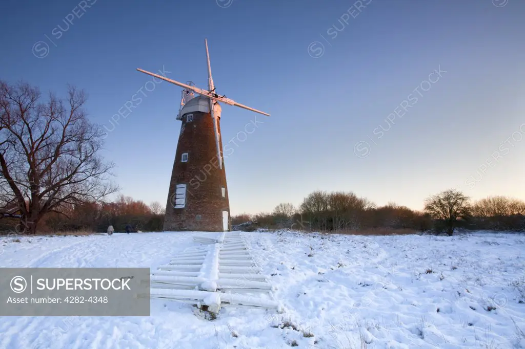 England, Norfolk, Billingford. Snow covering the ground around Billingford drainage mill. The main sails are on the ground undergoing restoration work.