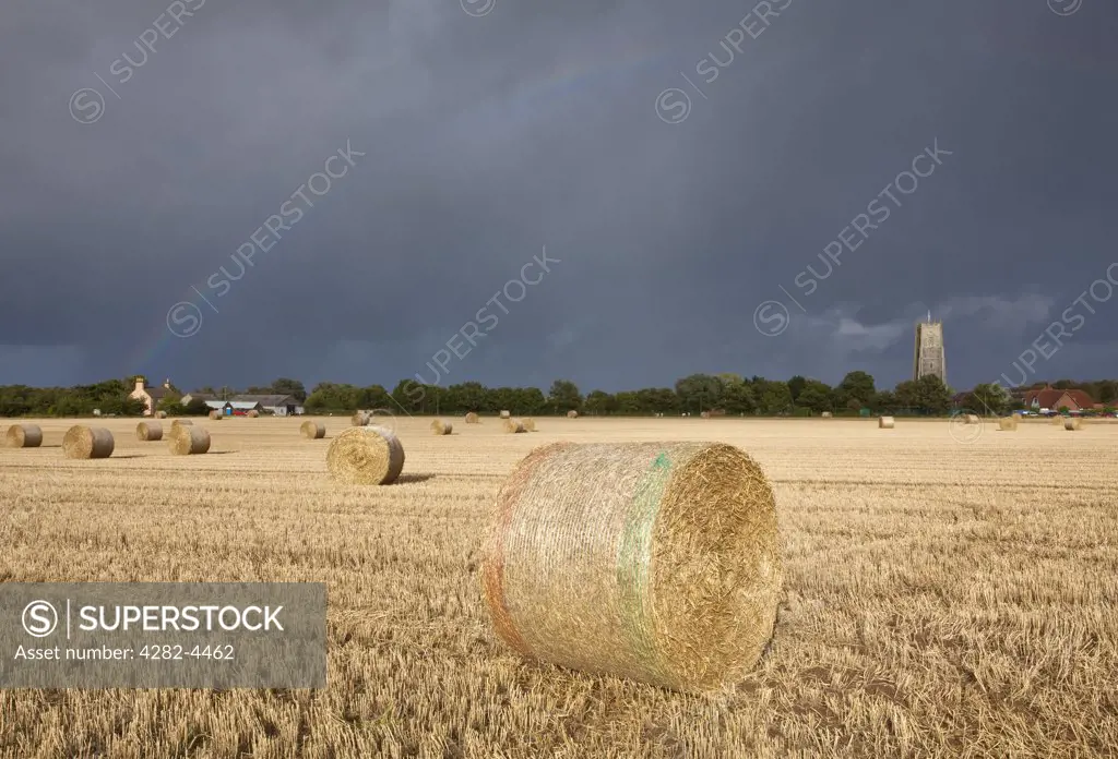 England, Norfolk, Winterton-on-Sea. View over bales of hay towards a rainbow over Holy Trinity and All Saints Church at Winterton-on-Sea.