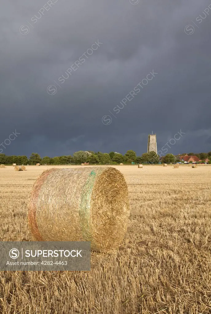 England, Norfolk, Winterton-on-Sea. View over bales of hay towards stormy clouds over Holy Trinity and All Saints Church at Winterton-on-Sea.