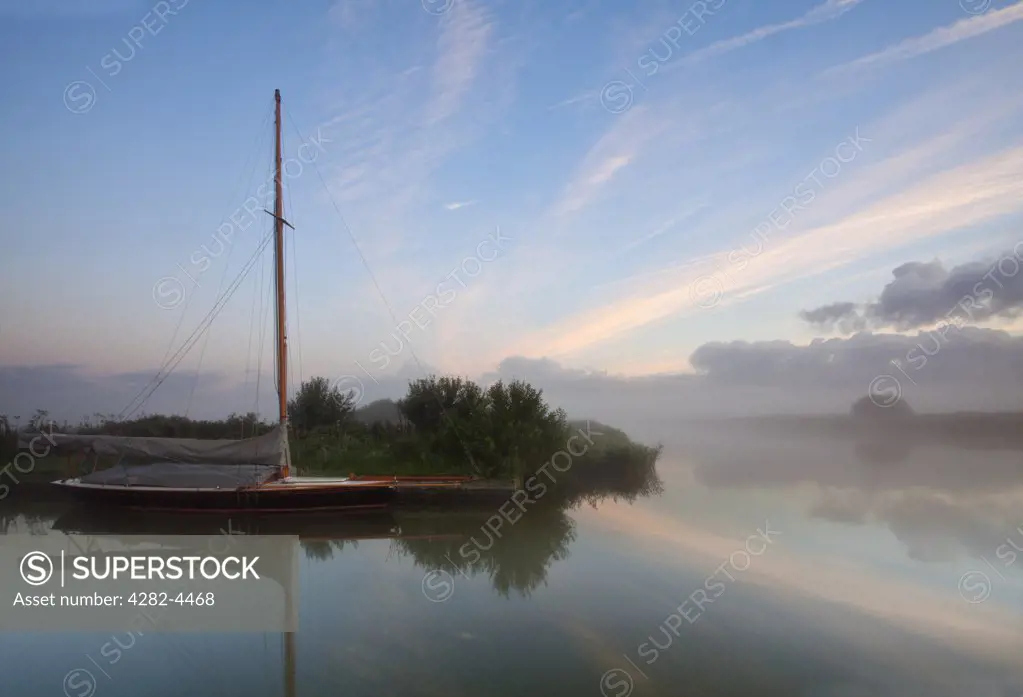 England, Norfolk, Norfolk Broads. A sailing boat in dawn mist on the River Thurne in the Norfolk Broads.
