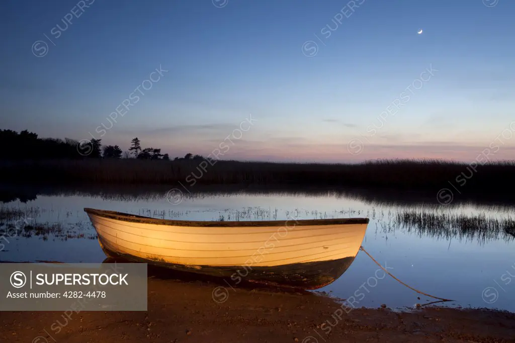 England, Norfolk, . A small rowing boat illuminated by torch light at night on the Norfolk Coast.