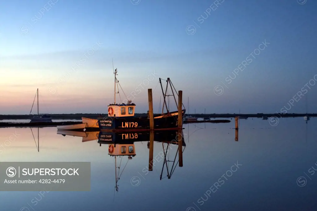 England, Norfolk, . Fishing boats reflected in still water at night on the Norfolk Coast.