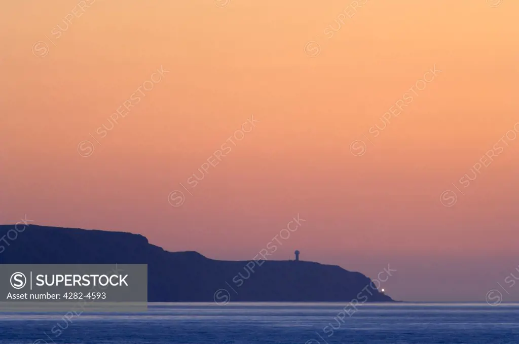 England, Devon, Westward Ho!. Hartland Point across Bideford Bay with a flash from the lighthouse. Hartland Point Lighthouse built in 1874, gives a guide to vessels approaching the Bristol Channel.