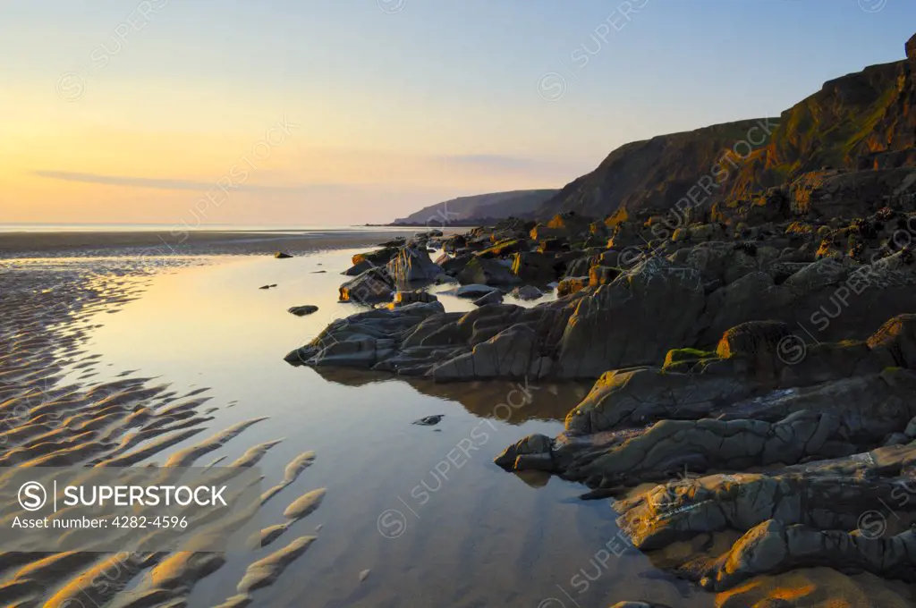 England, Cornwall, Bude. Sun setting over rocks and cliffs at Sandymouth beach. It is a large pebbled beach with lots of sand at lower tides when it connects up with other Bude beaches.