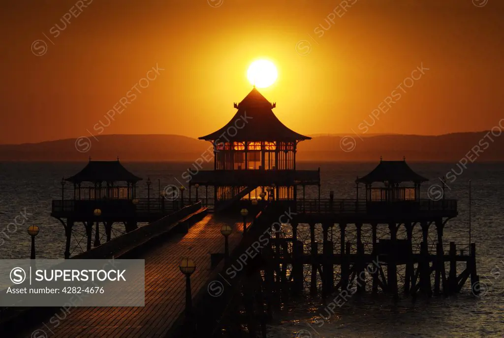 England, North Somerset, Clevedon. Sunset over the pier in the Bristol Channel at Clevedon. In 1913, the timber landing stage of the pier, which had deteriorated, was replaced by the present pre-cast concrete structure.