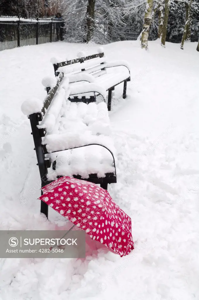 England, Somerset, Wrington. A red umbrella in the snow by a bench.