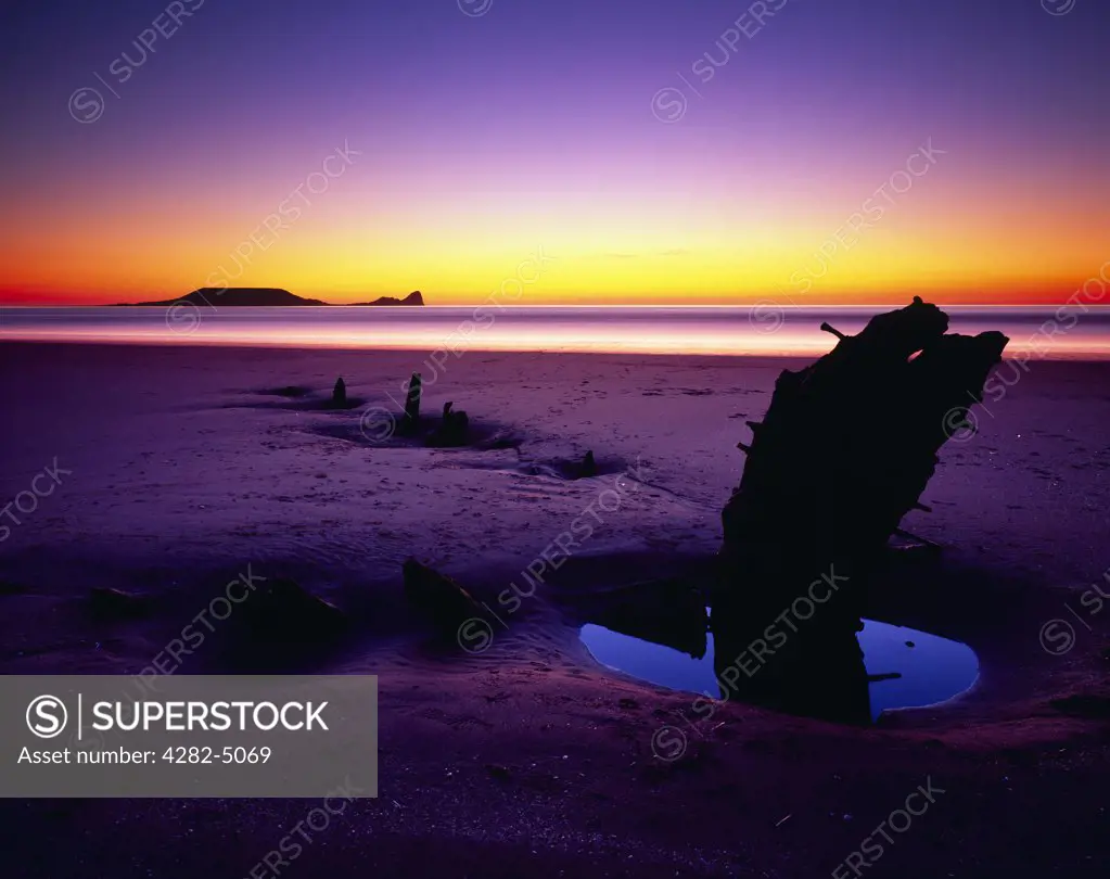 Wales, Swansea, Rhossili. The wreck of the Helvetia and Worms Head at Rhossili Bay on the Gower Peninsular at dusk.