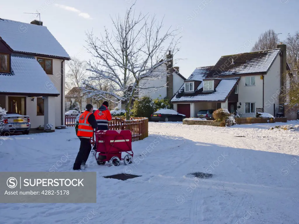 England, Somerset, Wrington. Two postmen trudging through snow on a road, delivering mail to houses.