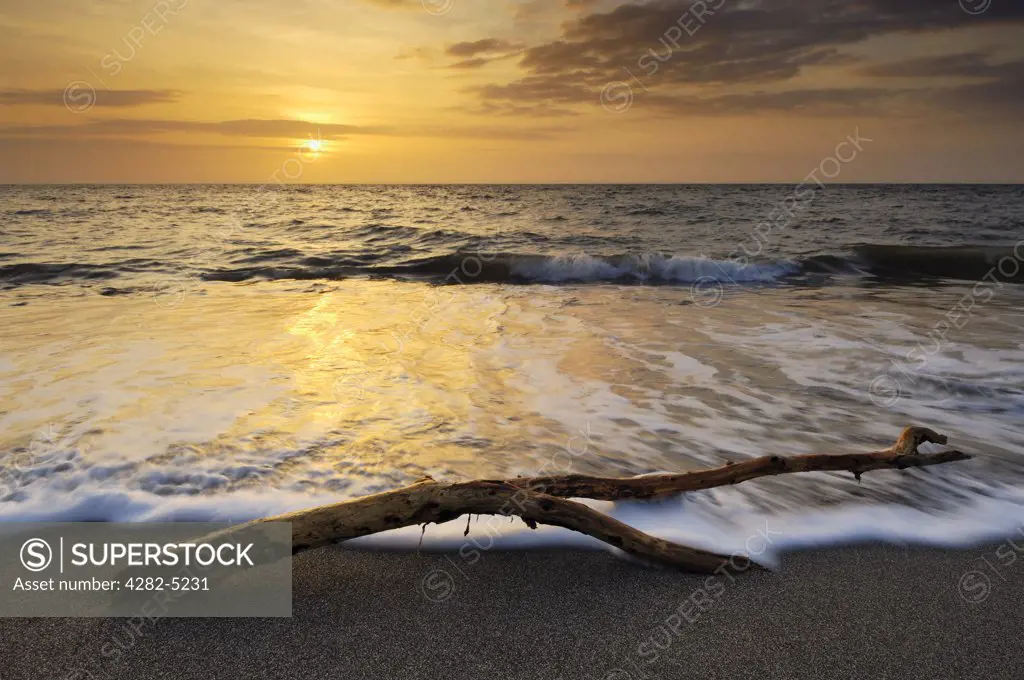 England, Devon, Westward Ho!. Waves washing past a piece of driftwood on the beach during sunset at Westward Ho! on the North Devon coast.