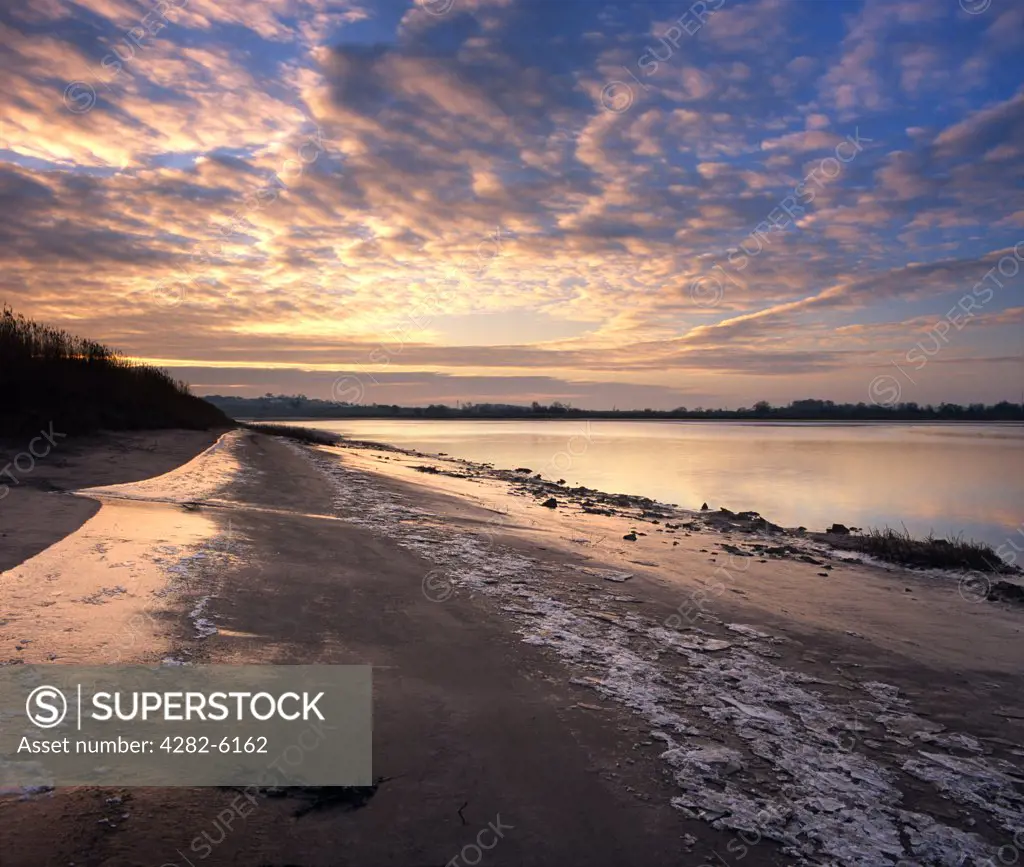 England, Gloucestershire, Westbury-on-Severn. A dawn sky is reflected in the water and icy shore of the River Severn.