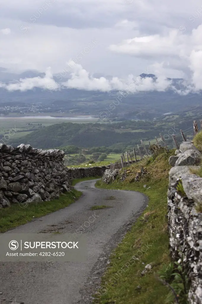 Wales, Gwynedd, near Talsarnau. Single track road winding downhill between traditional stone walls in the Snowdonia National Park.