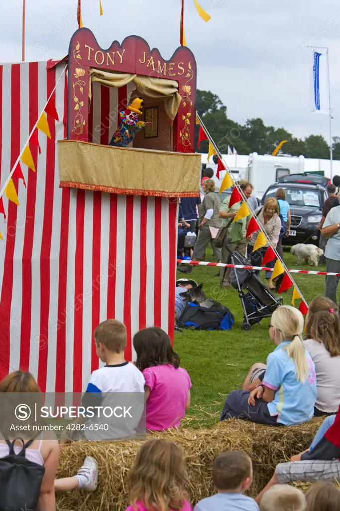 England, Gloucestershire, Frampton-on-Severn. Children sitting on bales of straw enjoying a Punch and Judy show at Frampton Country Fair.