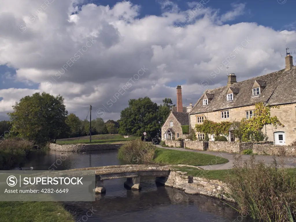England, Gloucestershire, Lower Slaughter. A clapper bridge across the River Eye and the Old Mill in Lower Slaughter.