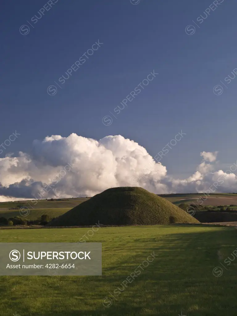 England, Wiltshire, Near Avebury. View of Silbury Hill, the tallest prehistoric human-made mound in Europe, against a bank of cloud on a clear evening.