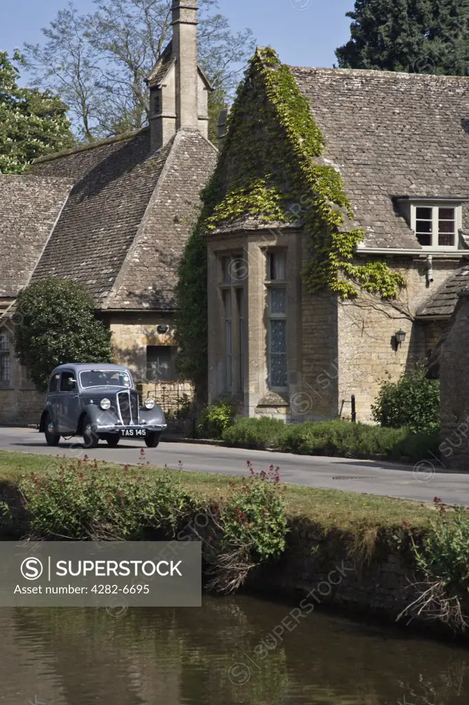 England, Gloucestershire, Lower Slaughter. A vintage car driving through the village of Lower Slaughter in the Cotswolds.