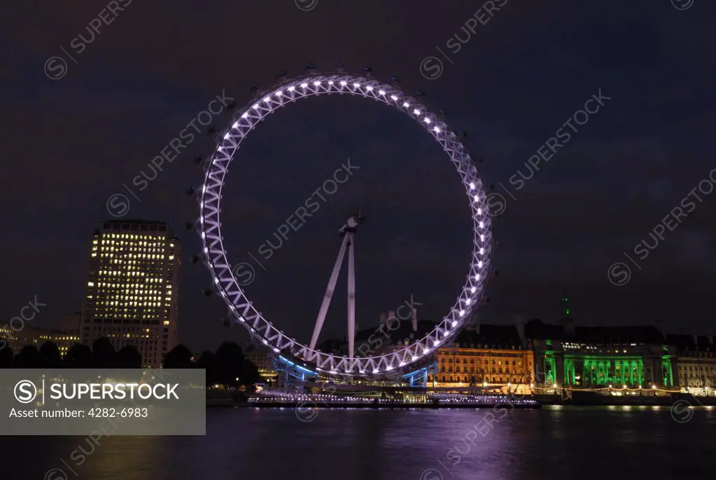 England, London, South Bank. View of the London eye at dusk with the river Thames in the foreground.