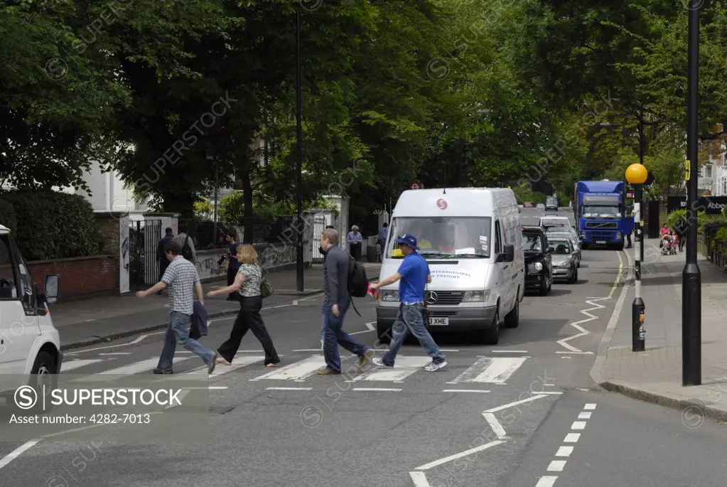 England, London, Abbey Road. Tourists walking across the famous Abbey Road pedestrian crossing with the Abbey Road studios in the background.