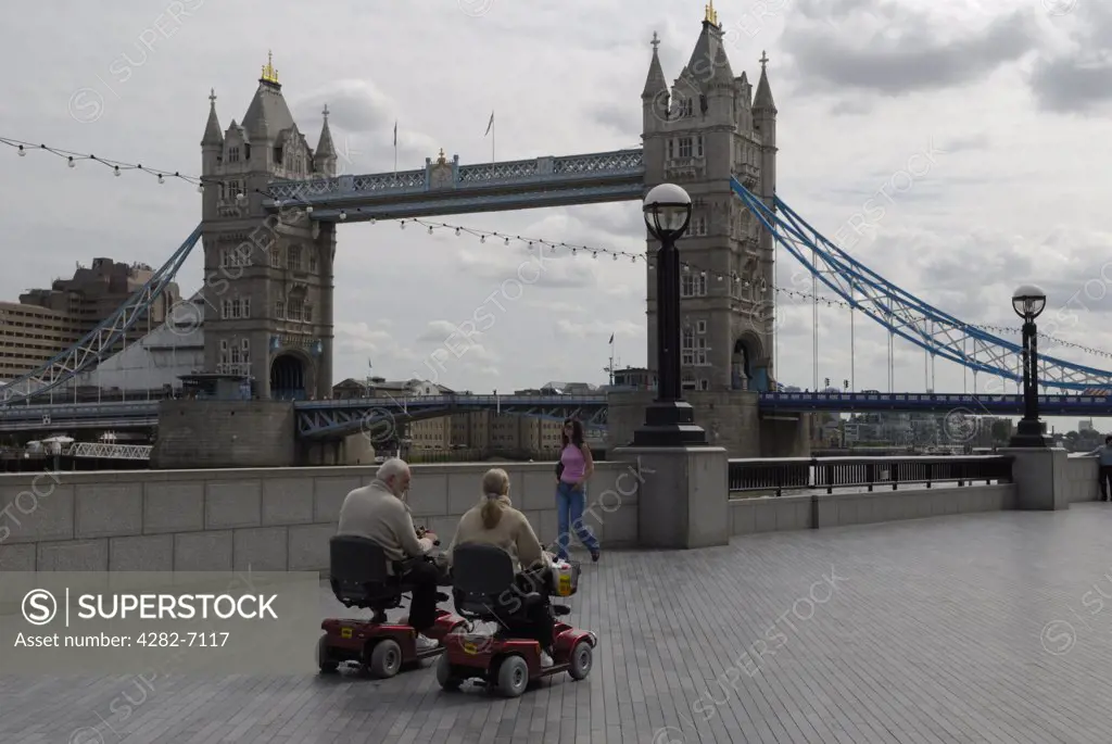 England, London, Tower Bridge. Elderly tourists using electric vehicles travelling along the embankment on the north side of the River Thames heading towards Tower Bridge.