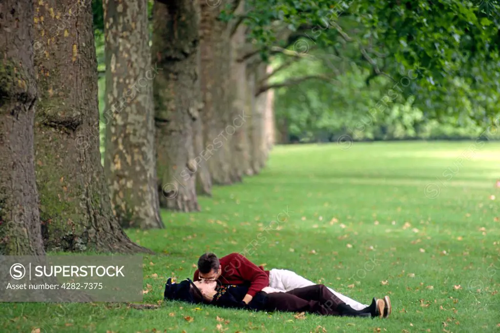 England, London, The Mall. A couple kissing on the lawns in St James's Park.