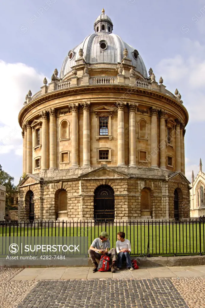 England, Oxfordshire, Oxford. Two students sitting in front of the Radcliffe Camera building. Originally a science library, it has become a reading room of the Bodleian Library.