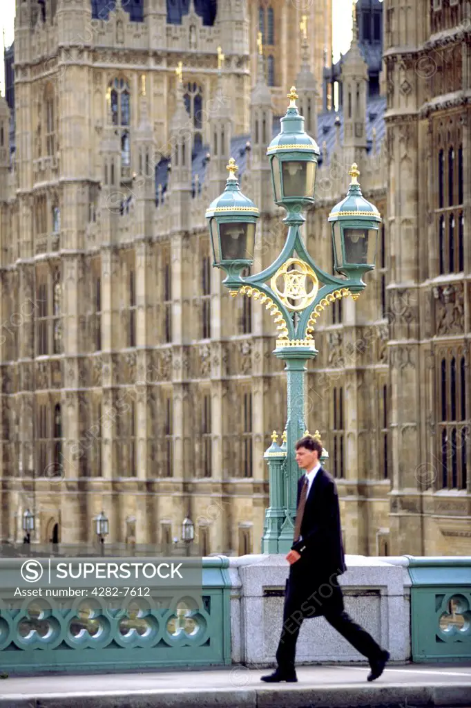 England, London, Westminster. A businessman walking over Westminster Bridge with the Houses of Parliament in the background.