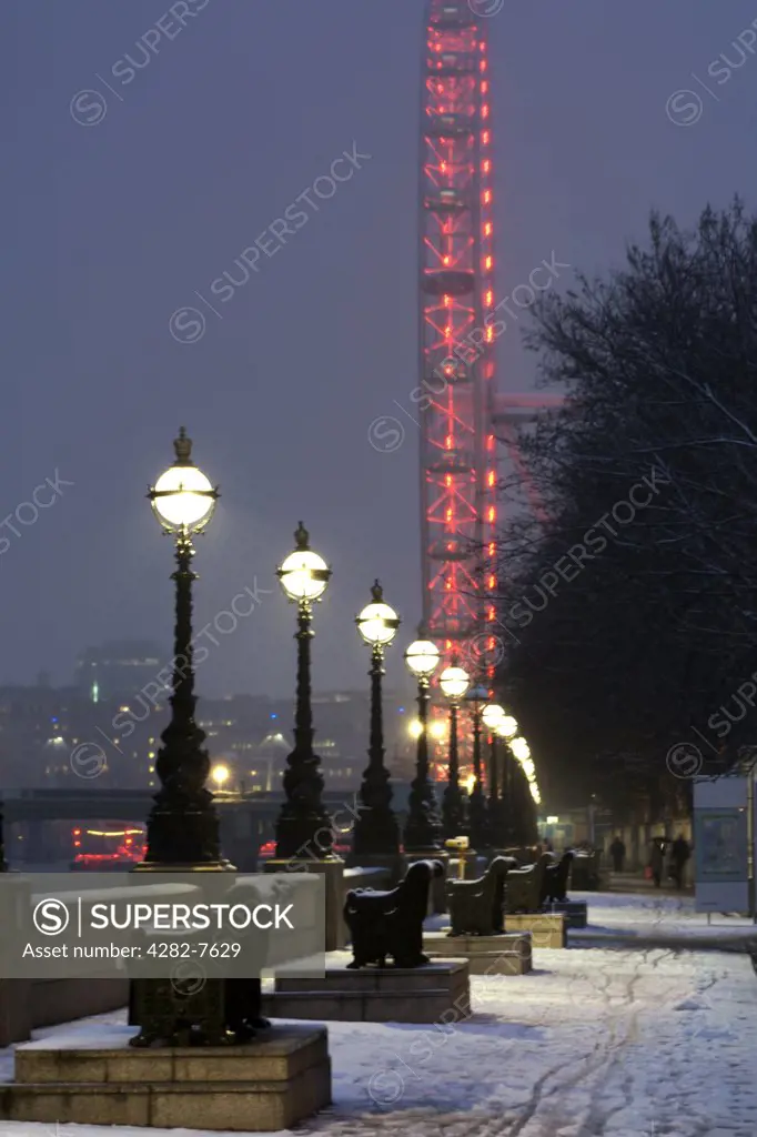 England, London, South Bank. An illuminated London Eye and River Thames embankment after a snowfall.