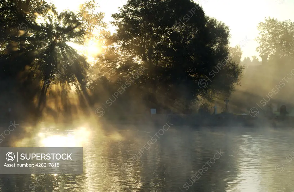 England, Buckinghamshire, Bisham. Sunrays through the mist at Bisham, with churchyard in background. Bisham is home to one of the Sport England's National Sports Centres, centred on Bisham Abbey.