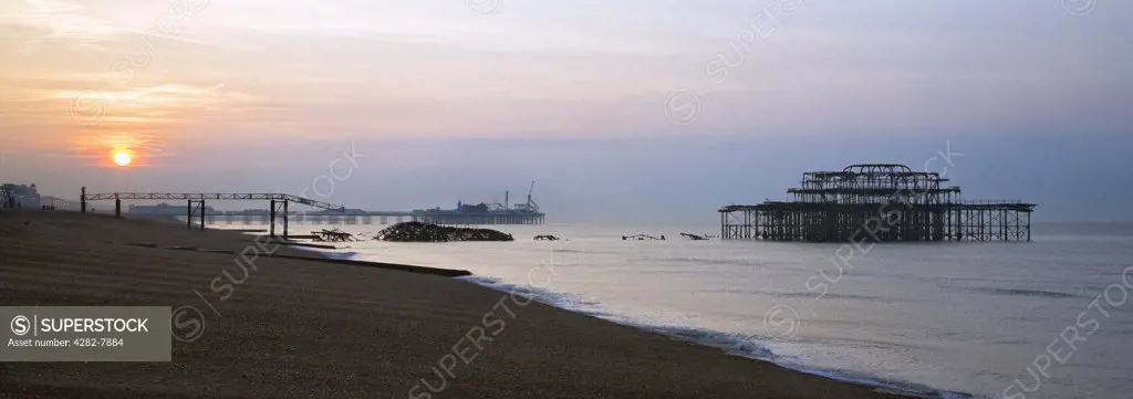 England, City of Brighton and Hove, Brighton. A view from the beach toward sunrise over the Brighton piers.