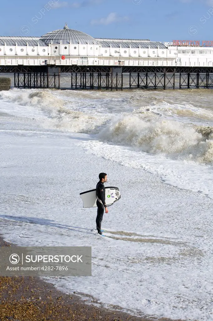 England, City of Brighton and Hove, Brighton. A lone surfer stands looking out to sea on Brighton beach.