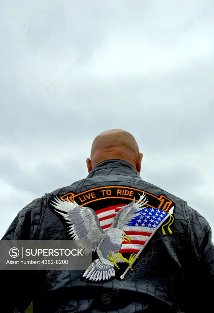 England, Cornwall, Falmouth. A biker wearing a leather jacket with an eagle carrying a stars and stripes flag emblem on the back.
