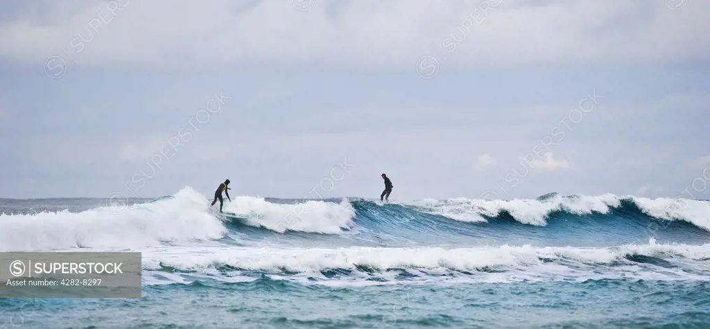 England, Cornwall, Sennen. Surfers riding the waves at Sennen Cove.