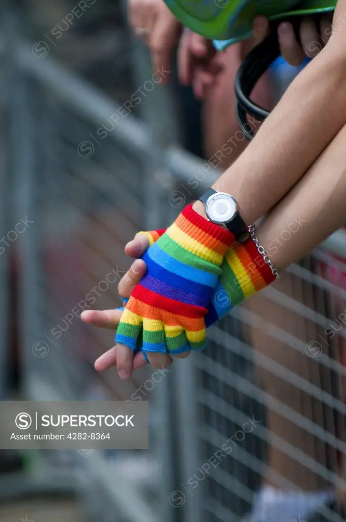 England, London. A gay couple holding hands wearing rainbow coloured fingerless mittens at the annual Pride London celebrations.