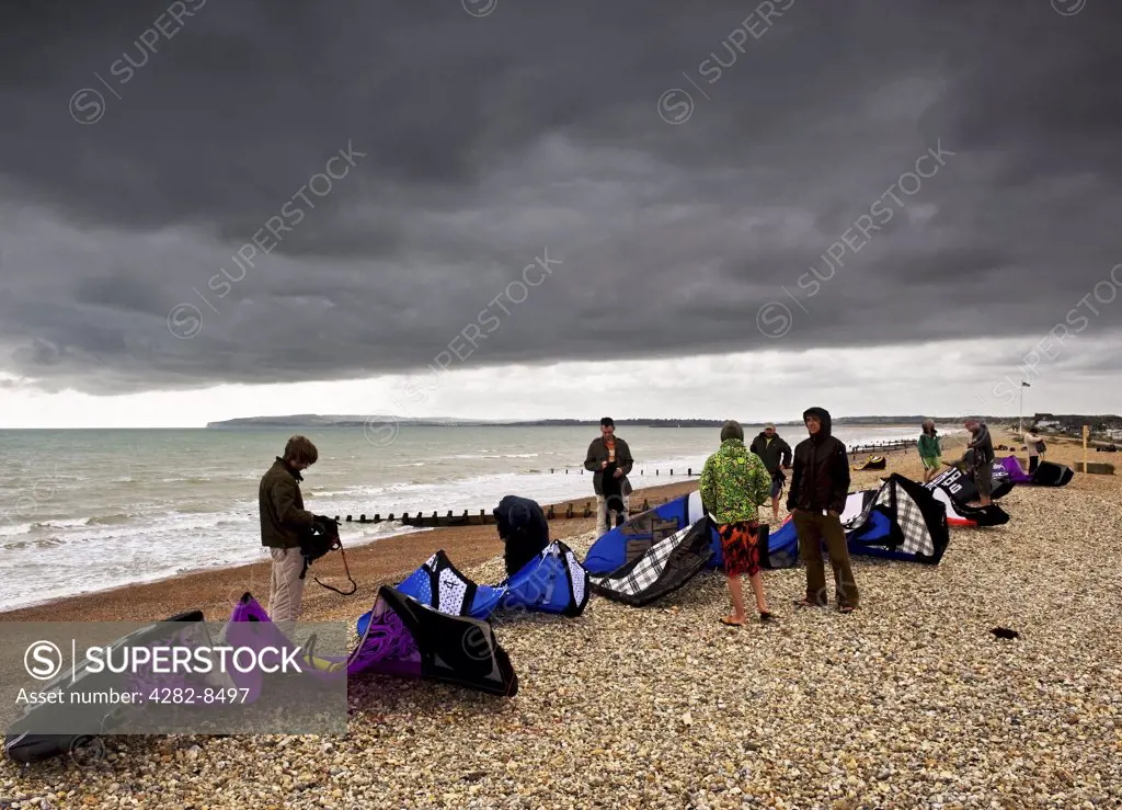 England, East Sussex, Camber. Novice parascenders learning how to repack their parasails beneath dark storm clouds on the beach at Camber Sands.