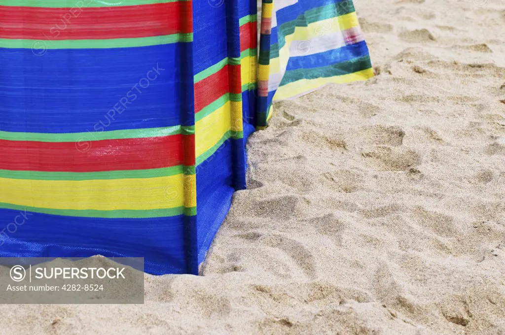 England, Cornwall, Sennen. A colourful striped windbreak on a sandy beach.