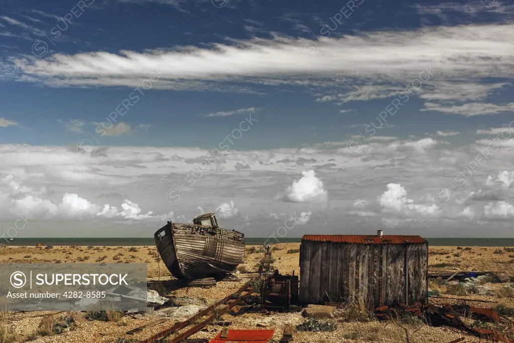 England, Kent, Dungeness. An abandoned wooden boat beached next to a fishermans wooden hut on the shingle beach at Dungeness.