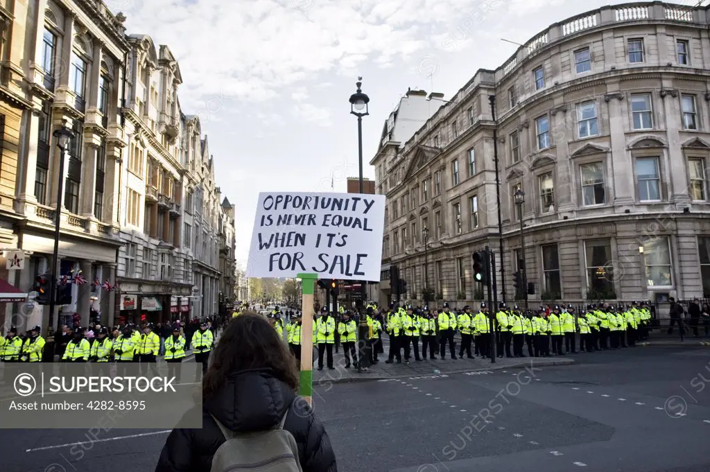England, London, Whitehall. A protester holding up a placard in front of a line of Metropolitan Police Officers at a demonstration against government education cuts in London.