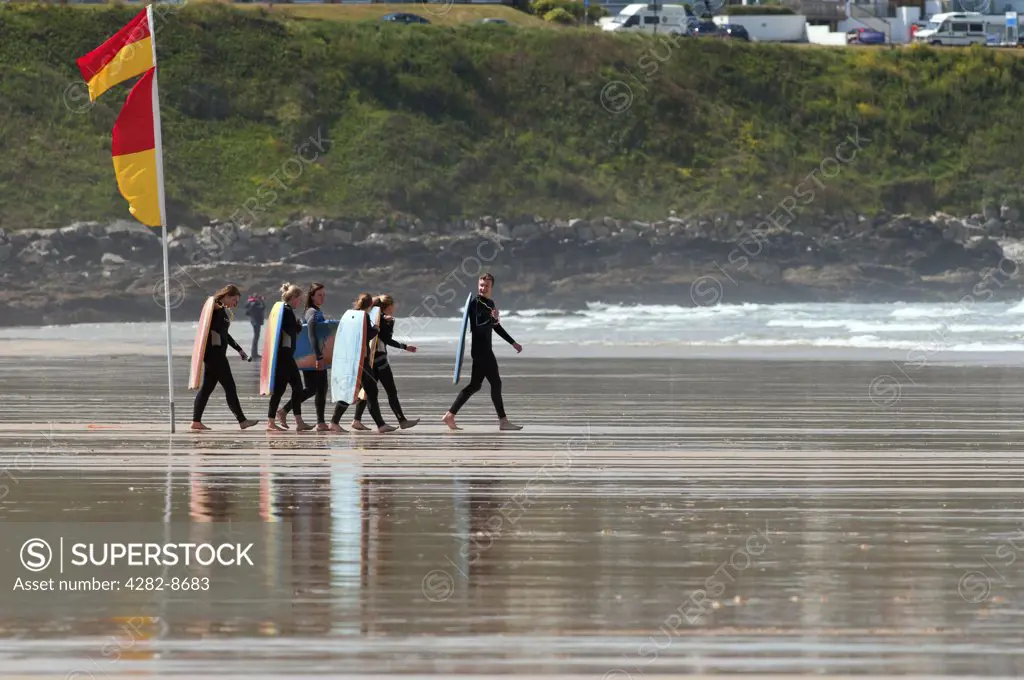 England, Cornwall, Newquay. A group of body boarders walking across Fistral Beach to the sea.
