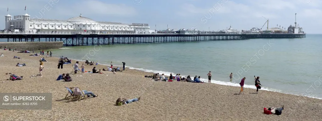 England, City of Brighton and Hove, Brighton. People relaxing on the pebble beach by Brighton Pier.