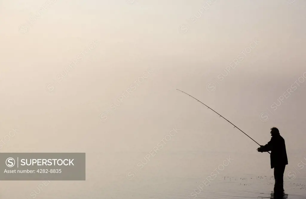 England, Cumbria, Bassenthwaite. The silhouette of a lone angler fishing in Bassenthwaite Lake in the Lake District.