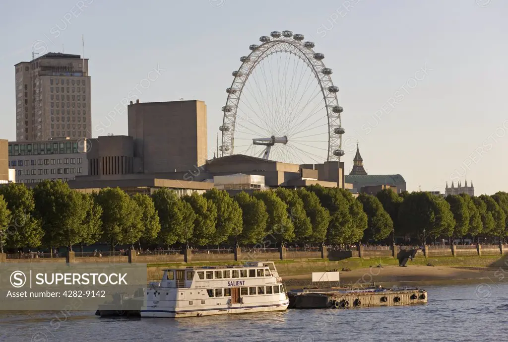 England, London, South Bank. A passenger boat moored on the River Thames with the London Eye in the background.