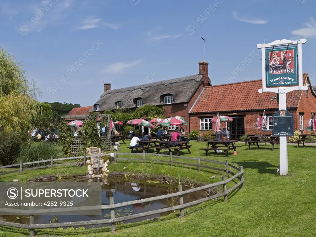 England, Norfolk, Woodbastwick. People sitting outside the thatched Fur and Feather pub and restaurant in the village of Woodbastwick, home of the award winning Woodforde's Broadland Brewery.