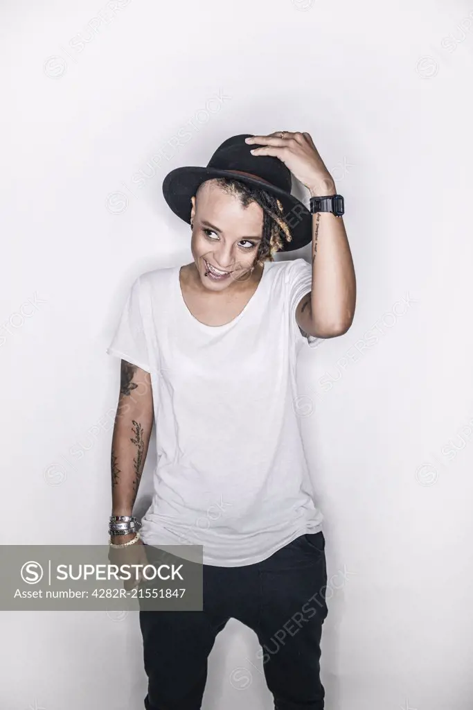 A young mixed race woman posing in a studio in a hat looking cool.