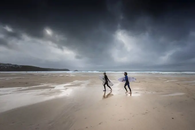 Surfers walking on Fistral Beach as dark gloomy storm clouds approach Newquay in Cornwall.
