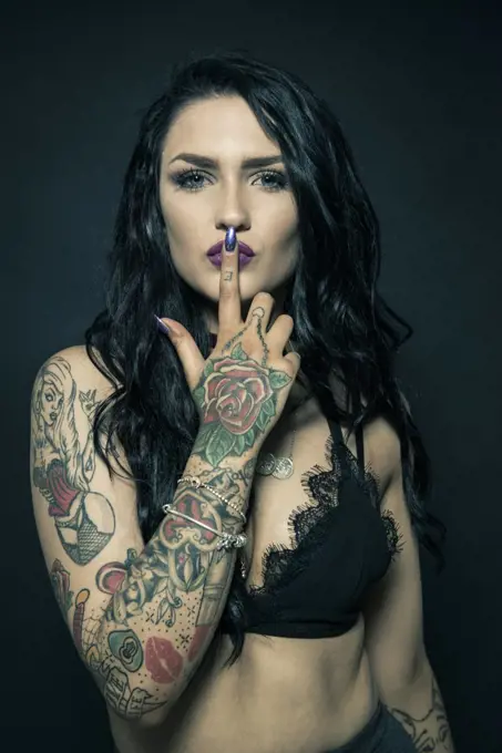 Studio portrait of a young woman with tattooed arms.