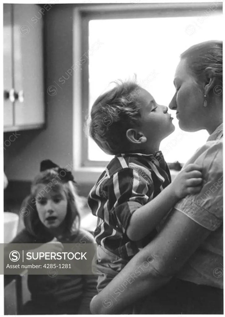 Younger brother gives mother a kiss while older sister looks on.