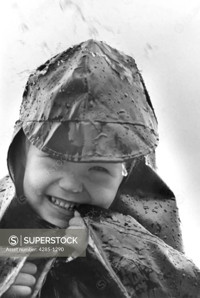 Young boy in rain hat and raincoat laughing in the rain.