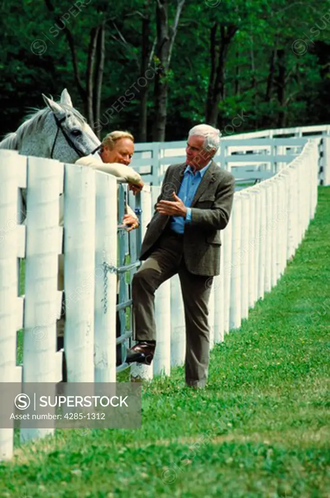 Horse buyer talking to horse trainer over white fence.
