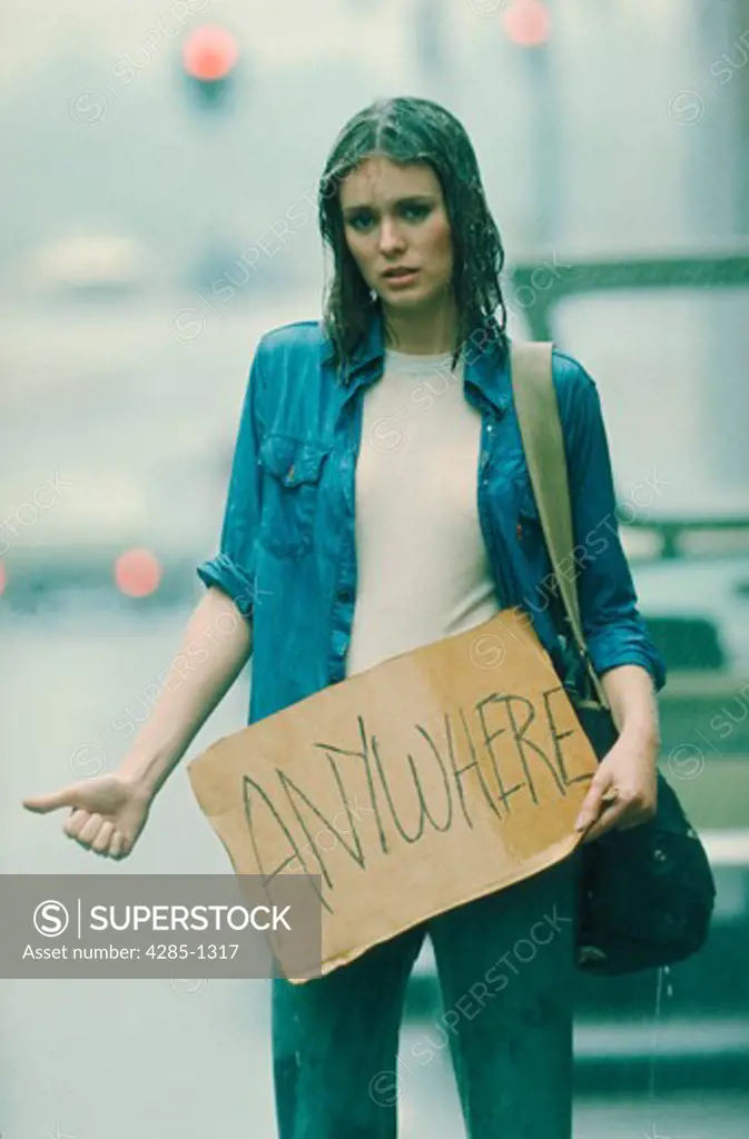 Desperate young woman hitchhiking in the rain to anywhere.
